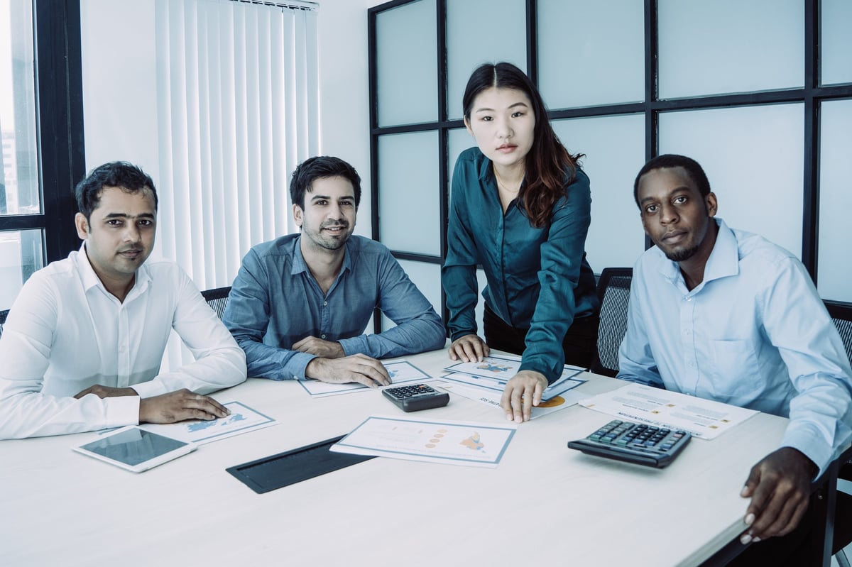 Portrait of multiracial business team of four posing at conference table. Young mix raced coworkers meeting, working on business plan and sharing ideas. Teamwork and brainstorming concept