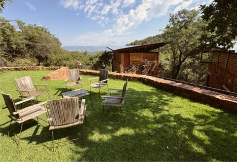 Wooden Adirondack chairs arranged on a green lawn with a rustic cabin and mountain views in the background