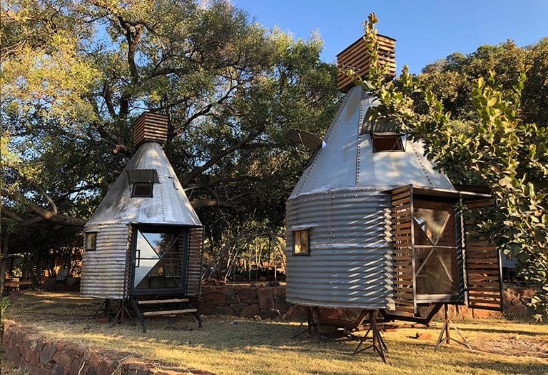 Two rustic cylindrical corrugated metal cabins with chimneys in a wooded area during autumn