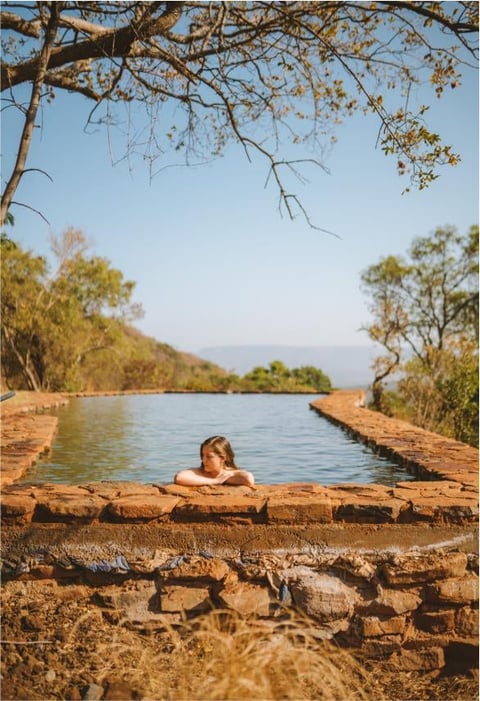 Person relaxing in a natural rock pool surrounded by trees and ocean views on a clear sunny day