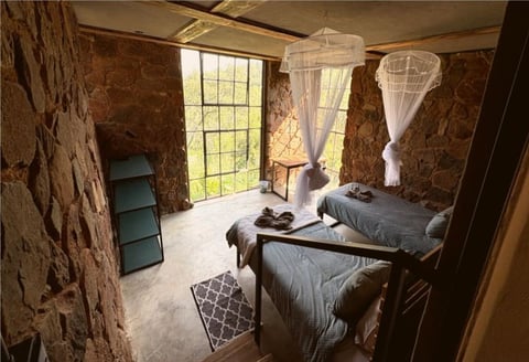 Historic stone bedroom with two twin beds draped with mosquito netting and a large window overlooking green landscape