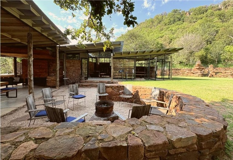 Modern cabin with stone firepit and seating area surrounded by green landscape and forested hills