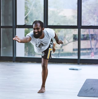 Man performing a standing leg lift exercise in a bright studio with large windows overlooking a cityscape