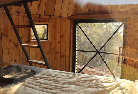 Rustic wooden bedroom interior with bed and cross-pattern windows overlooking forested landscape