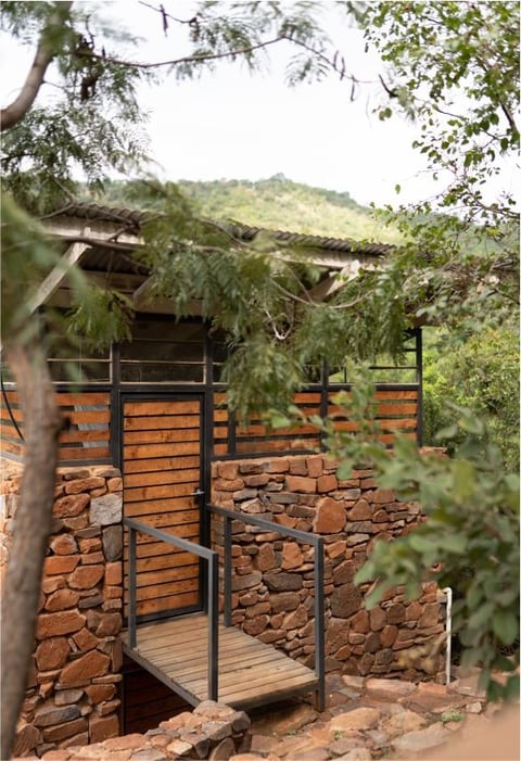 Modern cabin with wooden and stone exterior surrounded by trees and vegetation on a hillside