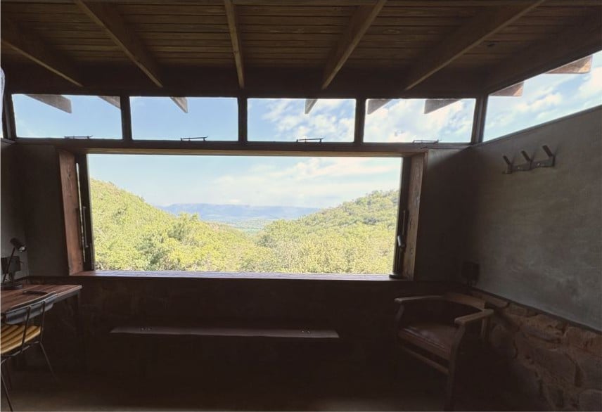 Interior view of rustic cabin with panoramic mountain valley vista through large window frame and skylights above