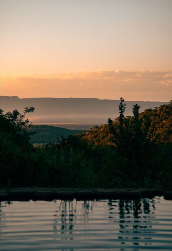 Serene sunset landscape with forested hills framing a calm river, misty valley and golden sky in background
