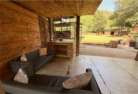 Covered patio with black seating, brick fireplace, and view of wooded ranch grounds